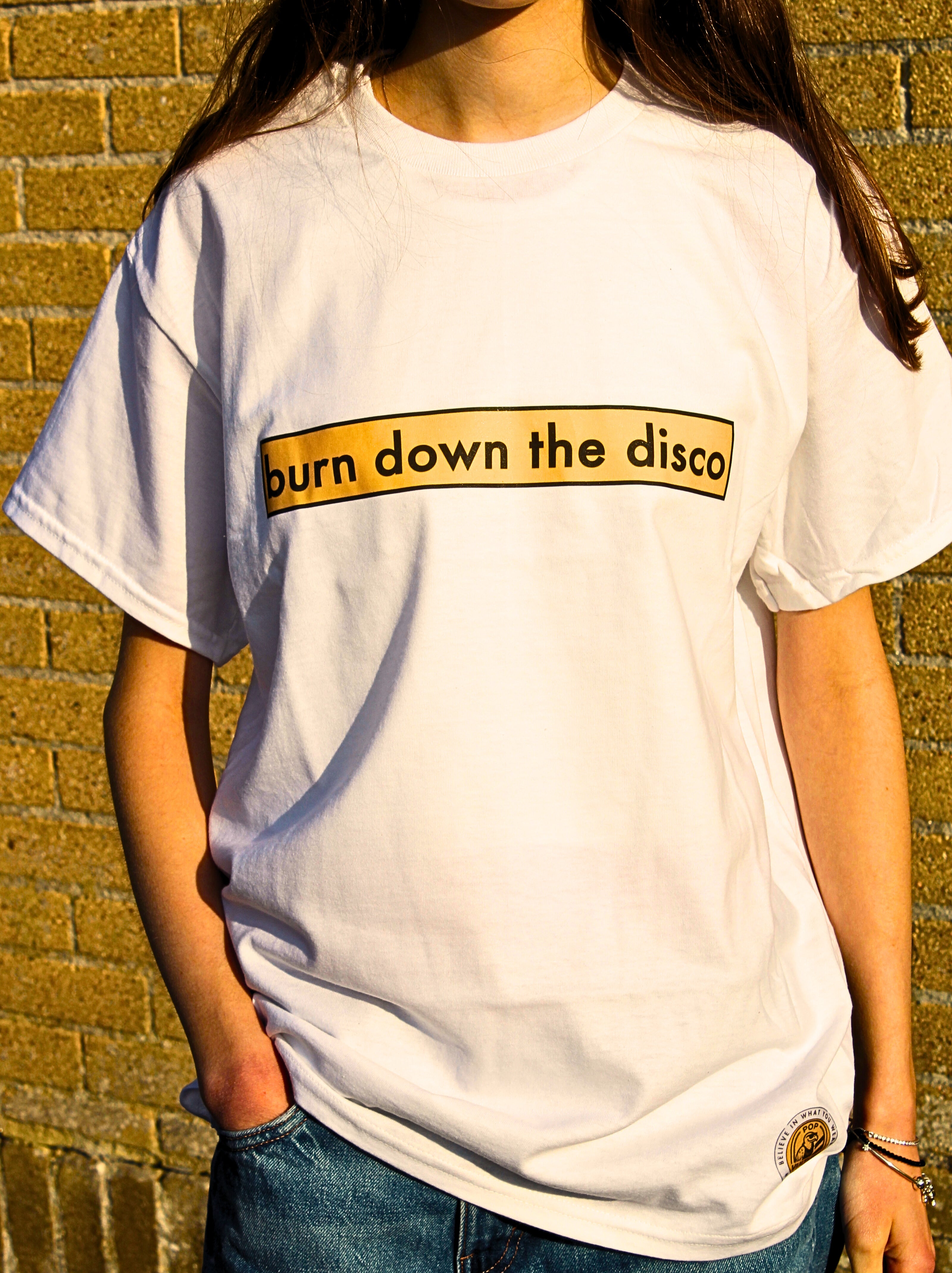 Person wearing a white t-shirt with 'burn down the disco' text against a brick wall.