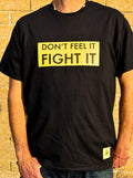Black t-shirt with yellow text 'DON'T FEEL IT FIGHT IT' worn by a person against a brick wall.