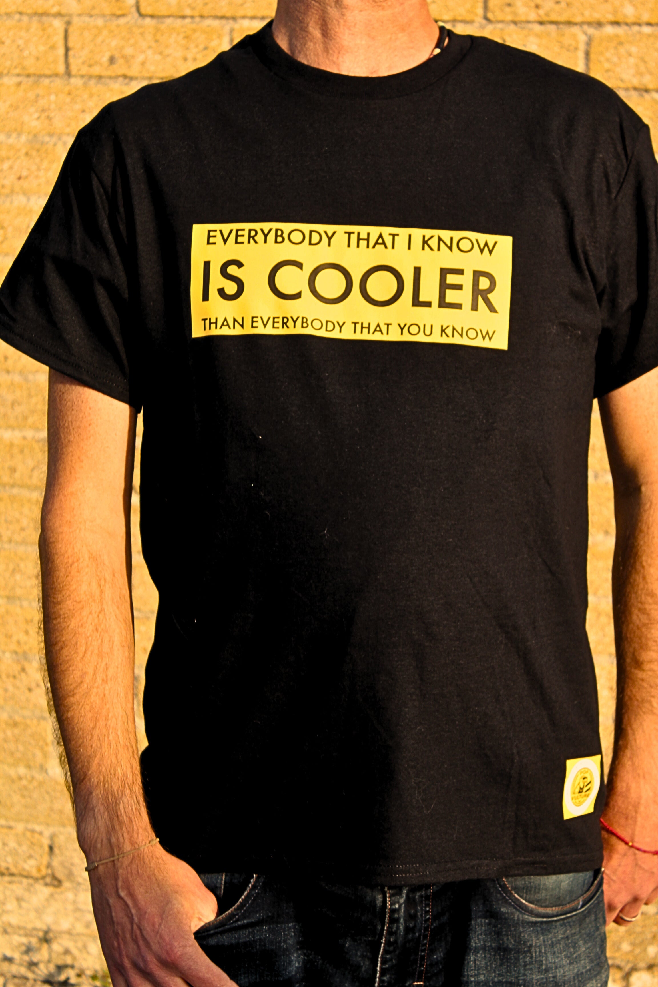 Person wearing a black t-shirt with yellow text against a brick wall.