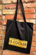 Black tote bag with yellow text against a brick wall