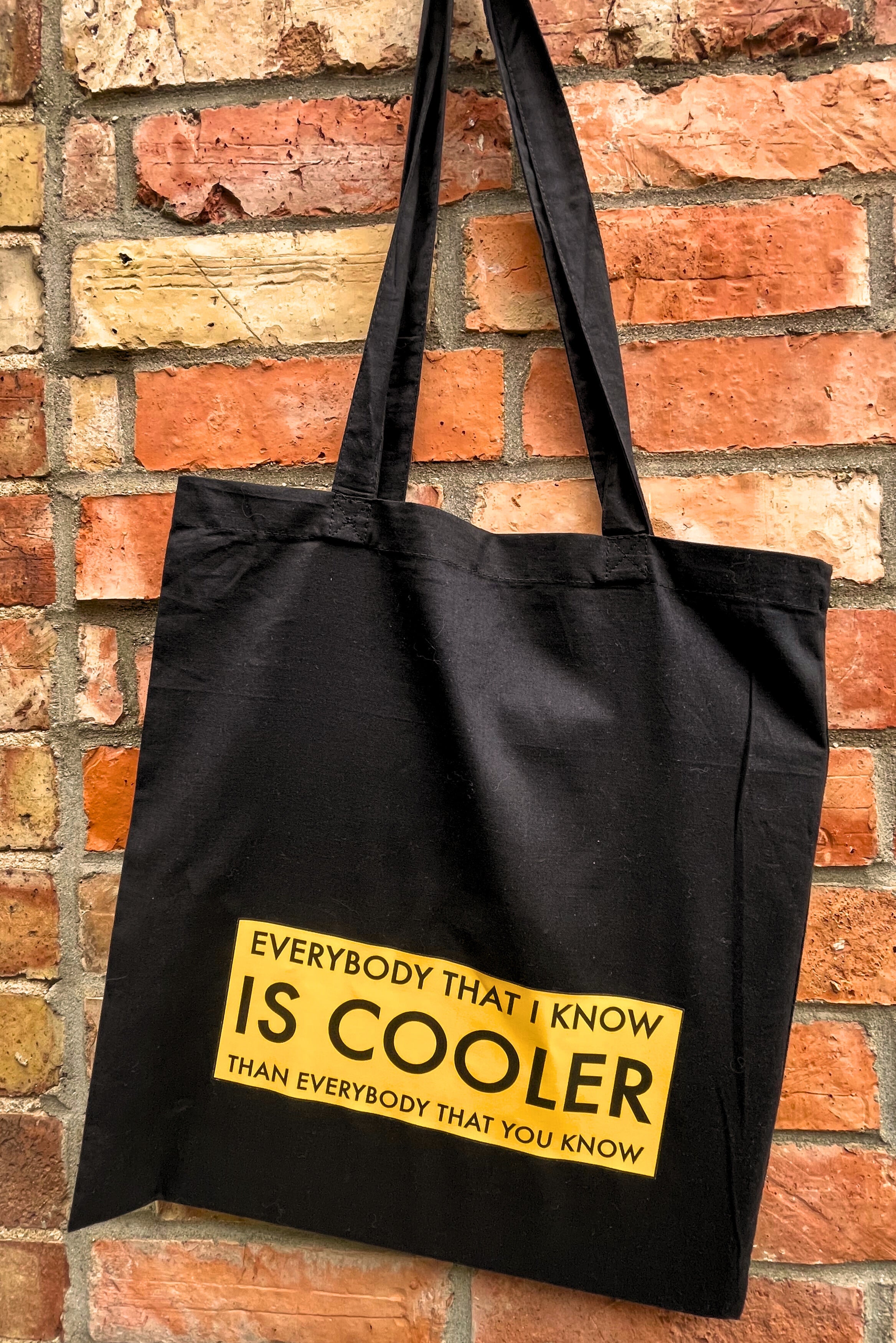 Black tote bag with yellow text against a brick wall