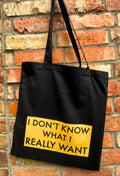 Black tote bag with yellow text against a brick wall