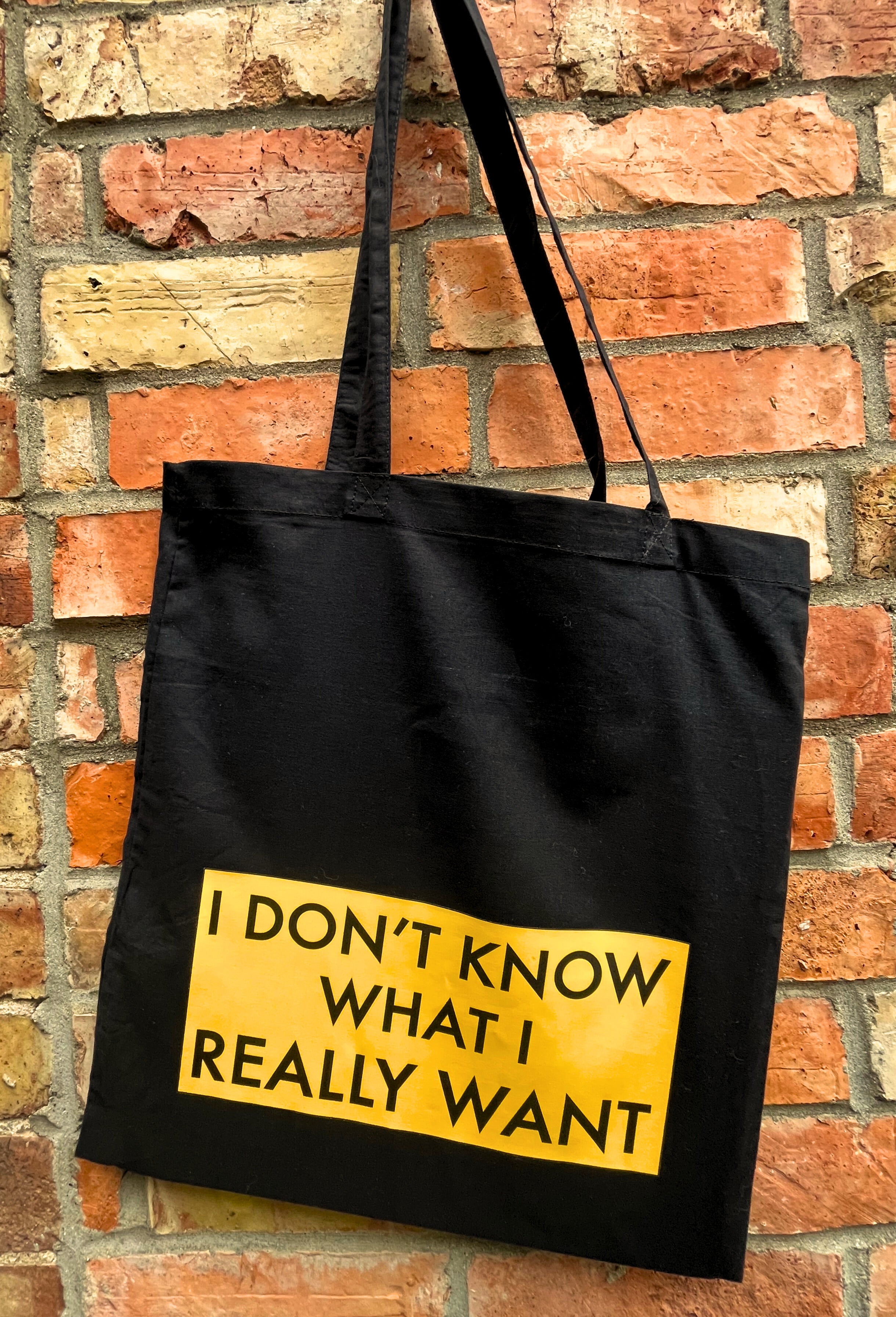 Black tote bag with yellow text against a brick wall
