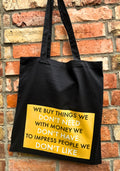Black tote bag with yellow text against a brick wall