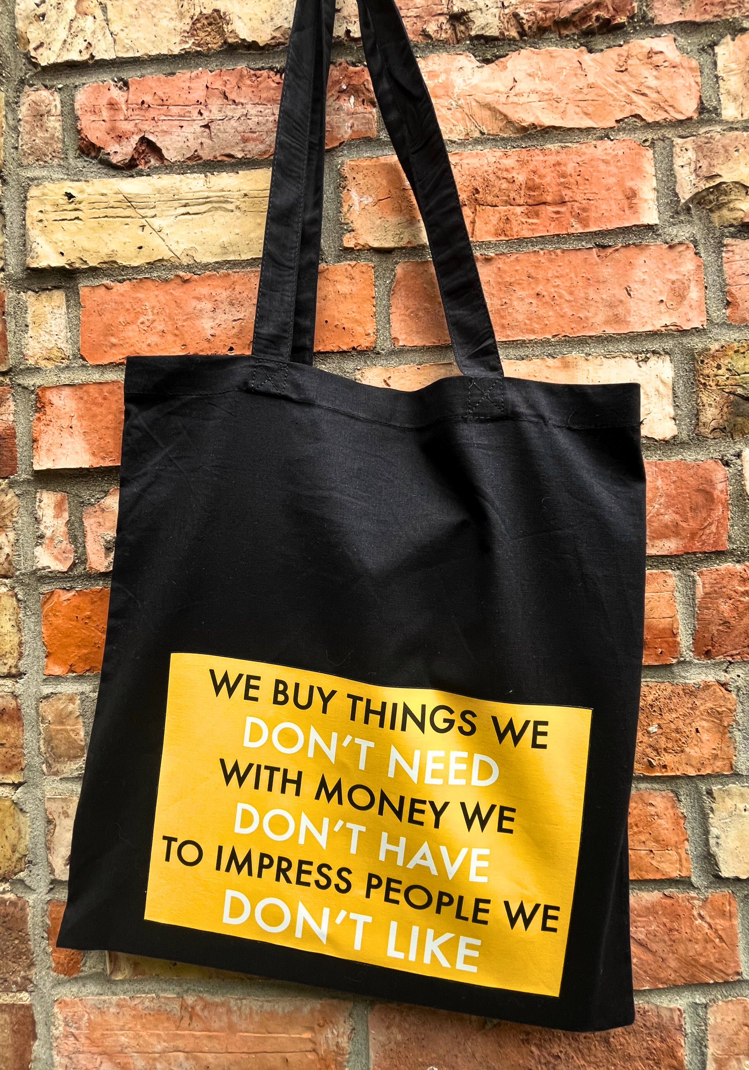 Black tote bag with yellow text against a brick wall